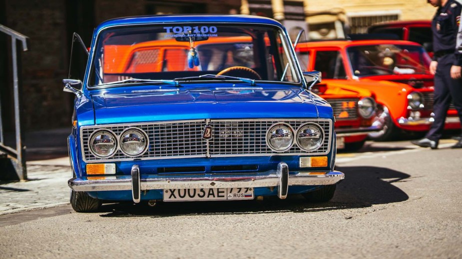 Blue lowrider parked in front of two red cars at a show.