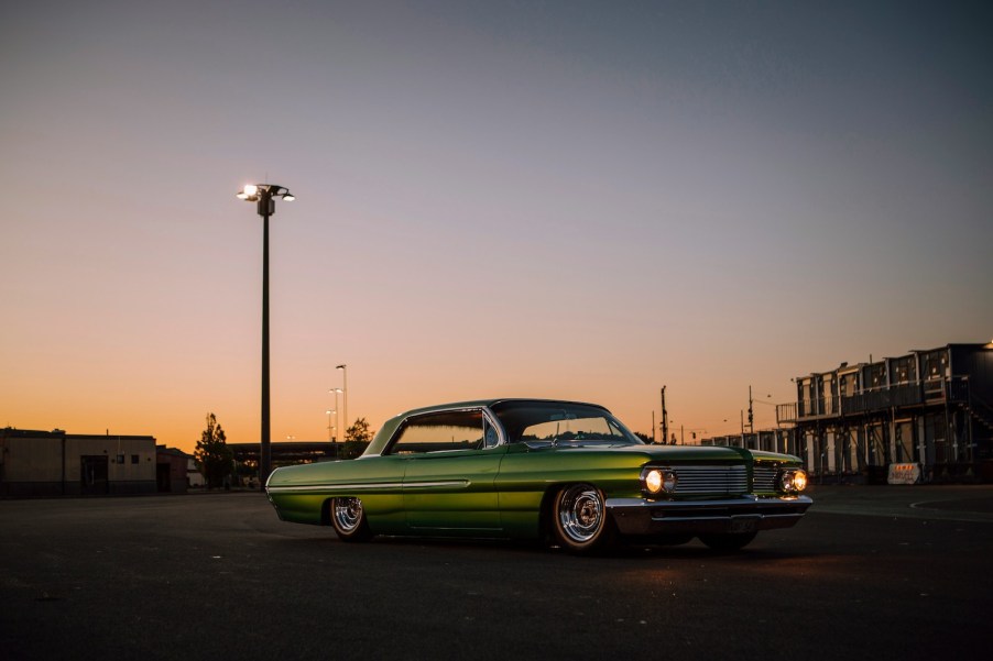 Green classic car on lowered suspension parked in front of the sunset.