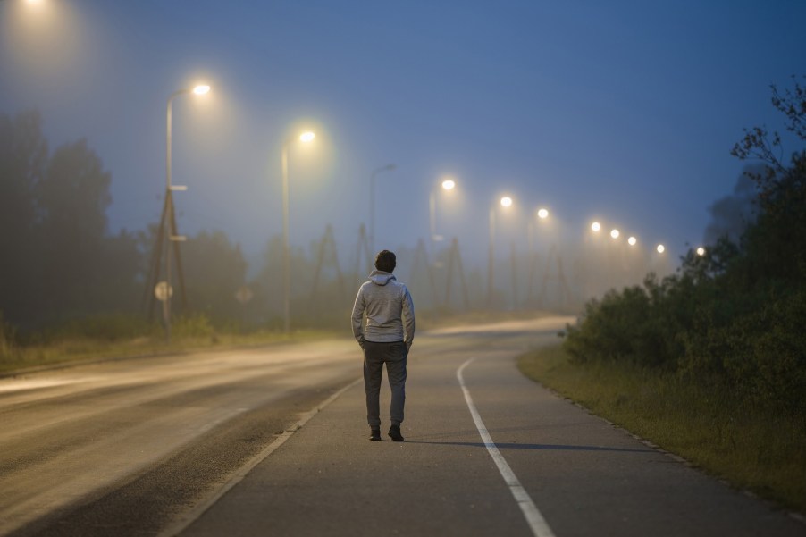 Young man walks under a row of street lights on a road at night.