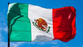 Green, white, and red Mexican flag flying in front of a blue sky