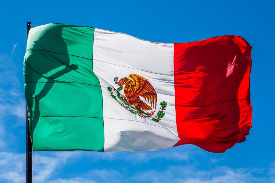 Green, white, and red Mexican flag flying in front of a blue sky