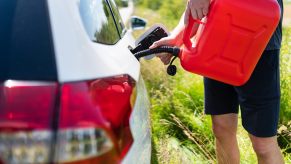 A man uses a red gas can to refill the empty fuel tank of a car.