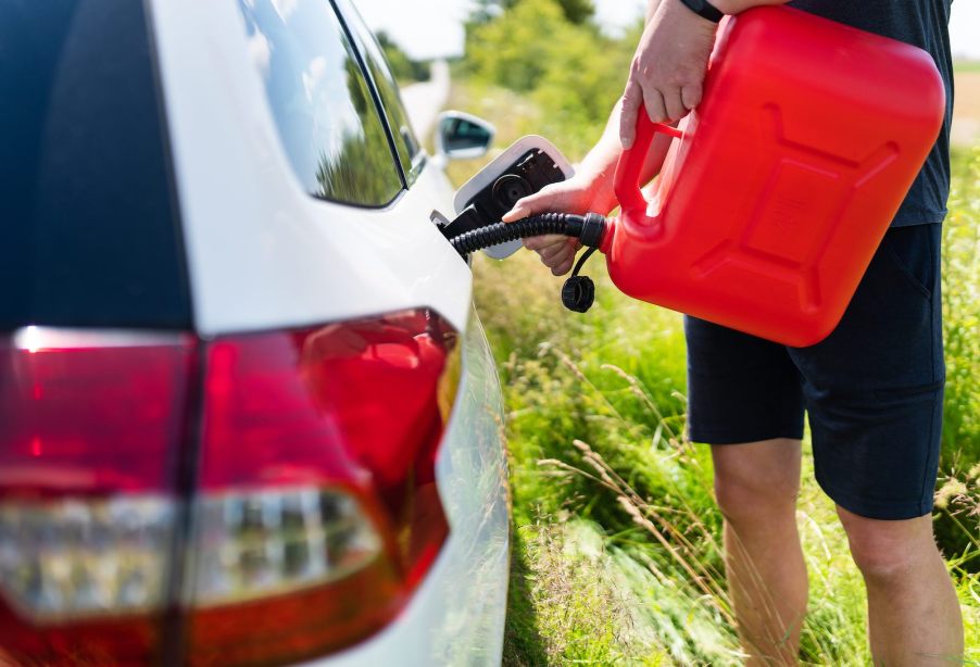 A man uses a red gas can to refill the empty fuel tank of a car.