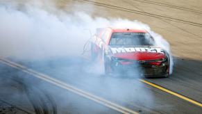 Red NASCAR car doing burnouts on the track