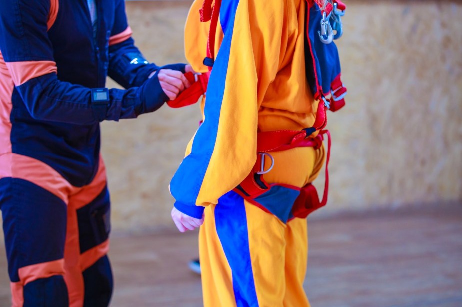 A parachute instructor tightens the harness straps another skydiver wears.