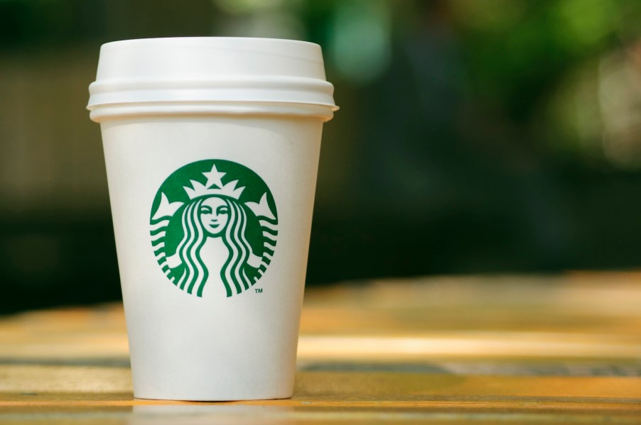 A white Starbucks to-go cup sitting on a wood counter.