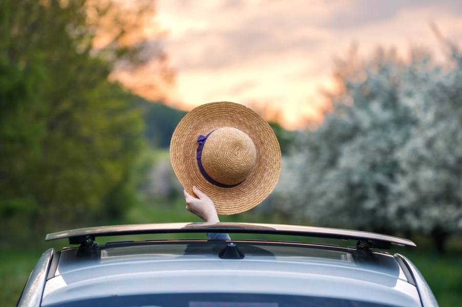 A passenger waves their hat through an open sunroof in a car.