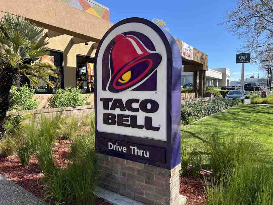 The "Taco Bell Drive Through" sign outside a restaurant, plants visible in the background.