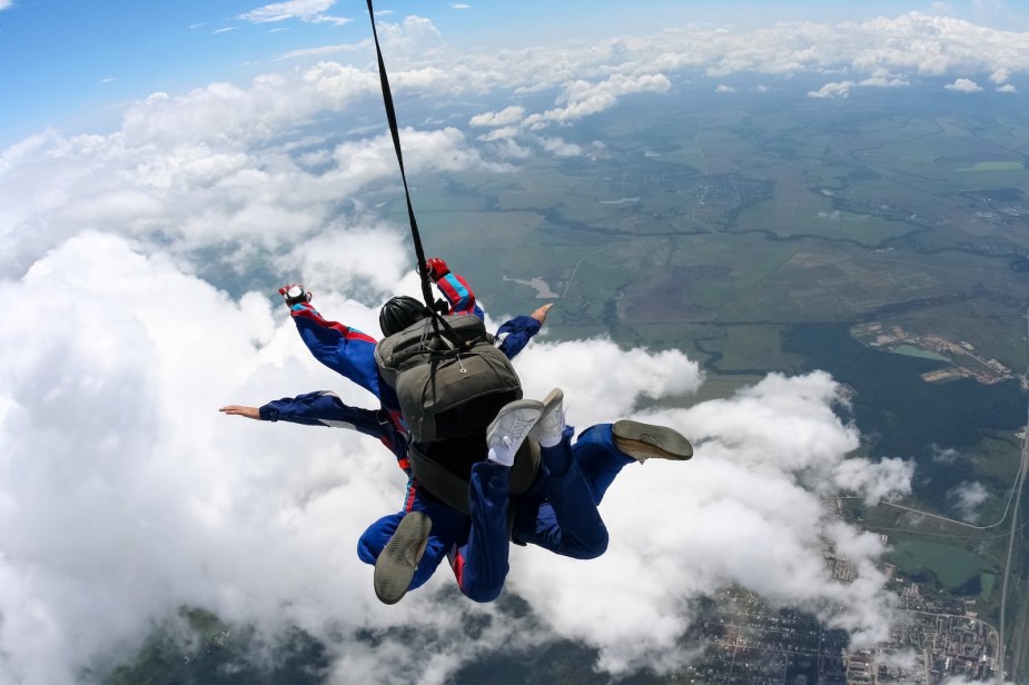 Two skydivers tethered together parachute towards the ground.