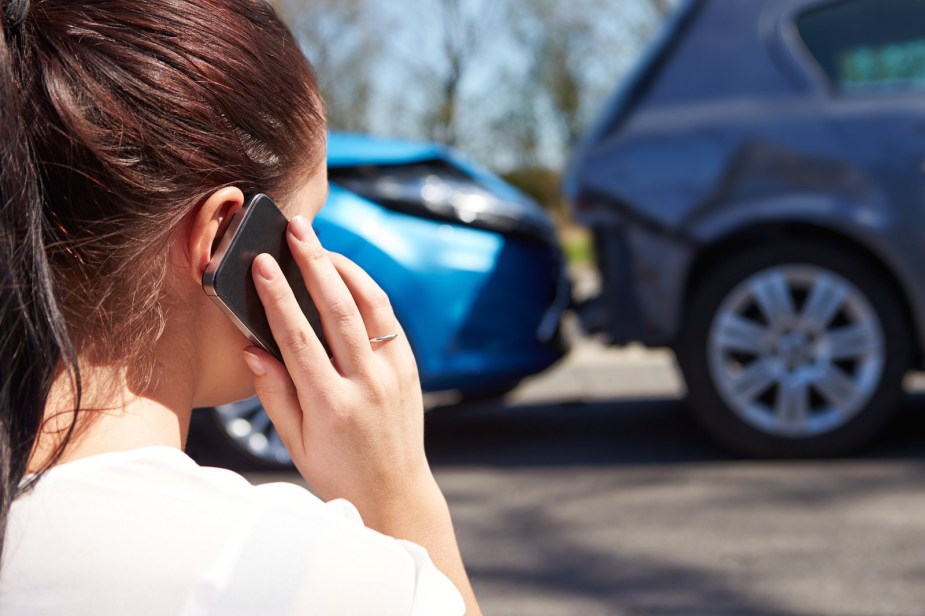 Woman holds up her phone while looking at an auto accident.