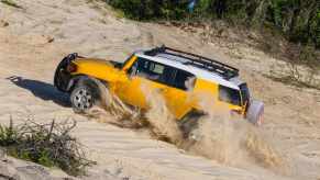 Yellow Toyota FJ Cruiser SUV drives up sand dunes on the beach.