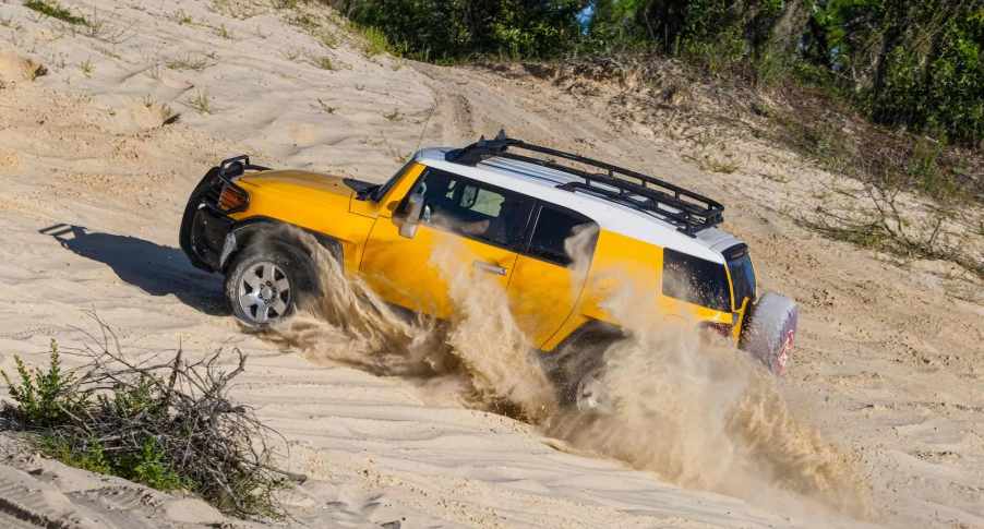 Yellow Toyota FJ Cruiser SUV drives up sand dunes on the beach.