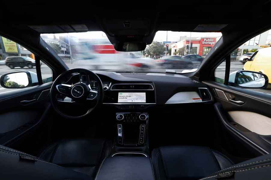 A driverless Waymo car is shot from the back interior of the vehicle while traffic passes in front of it