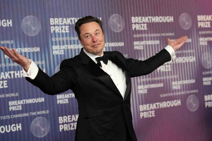 Elon Musk Tesla CEO wearing a black tuxedo at an event with arms open wide smirking closed smile