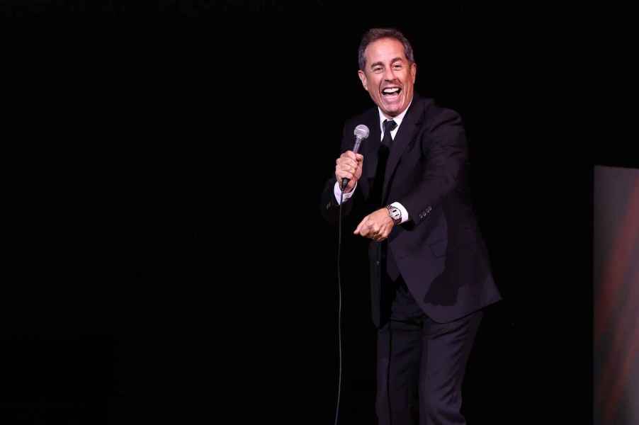 Comedian Jerry Seinfeld on stage performing in black suit