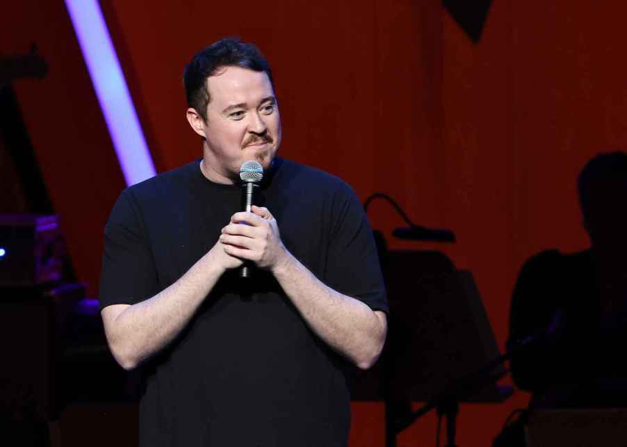 Comedian Shane Gillis star of show 'Tires' holding a mic on stage using two hands