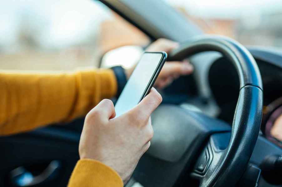 A set of arms wearing mustard yellow shirt driving a car while texting on cell phone showing distracted driving and violation of hands-free states laws