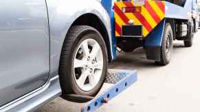 A blue tow truck carries a silver car shown in right rear side closeup angle view