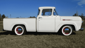 A white vintage 1960 Ford F100 pickup truck sitting in right profile view on grass blue sky in background