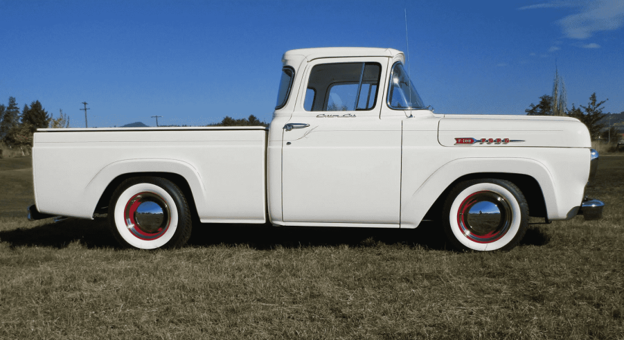 A white vintage 1960 Ford F100 pickup truck sitting in right profile view on grass blue sky in background