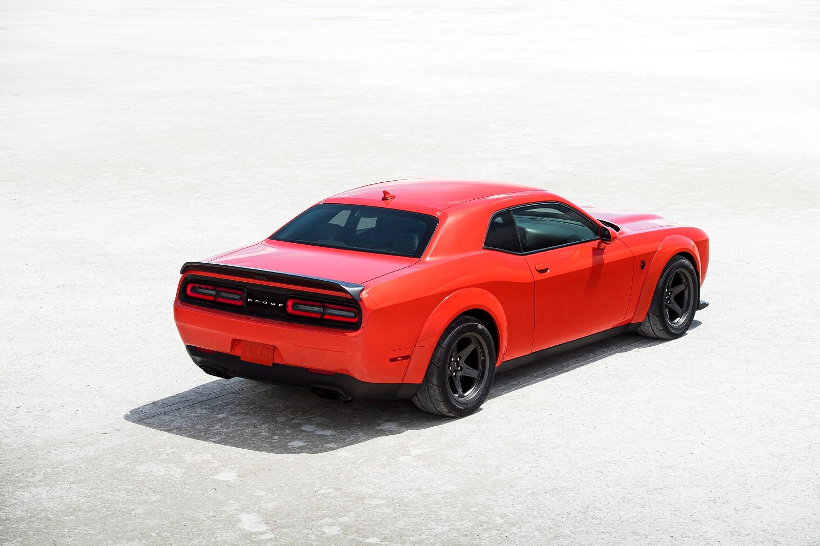 A red dodge challenger parked on a bright light surface in right rear angle view