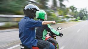 A motorcycle rider receives information from a passenger with a pointed finger.