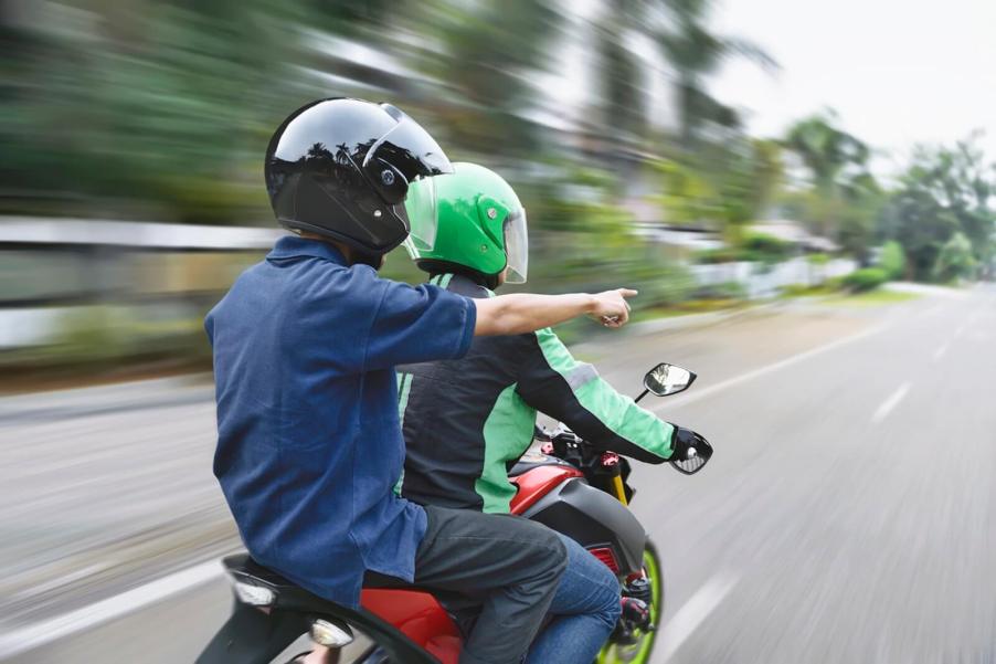 A motorcycle rider receives information from a passenger with a pointed finger.