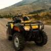 Bright yellow ATV parked on a dirt road, mountains in the background.