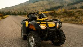 Bright yellow ATV parked on a dirt road, mountains in the background.