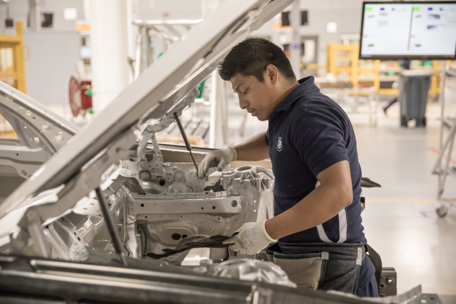 Factory worker stands under the open hood of a 3 Series sedan in BMW's Mexico plant.