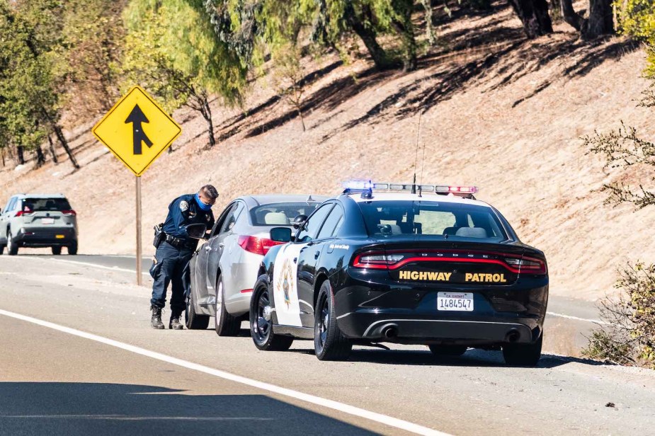 California highway patrol officer talking to the driver of a speeding car by the side of the highway.