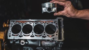 Hand holding a piston near a polished V8 engine block.