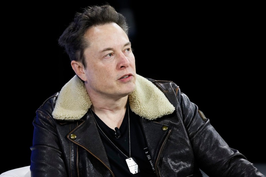 Elon Musk wearing a leather jacket on stage at a press conference