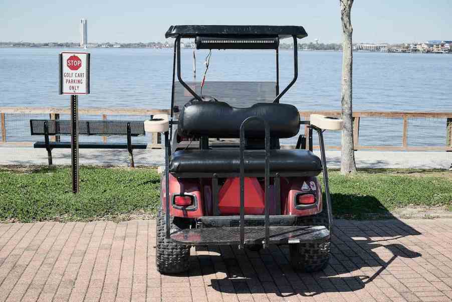 The back of a golf cart parked facing a lake, next to a "golf cart parking only" sign.