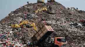 Workers use equipment to move trash around a landfill.