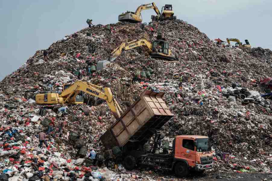 Workers use equipment to move trash around a landfill.