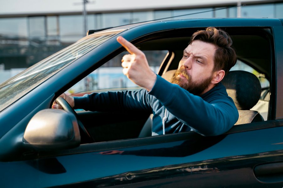 Frenchman pointing his finger out his window during traffic.