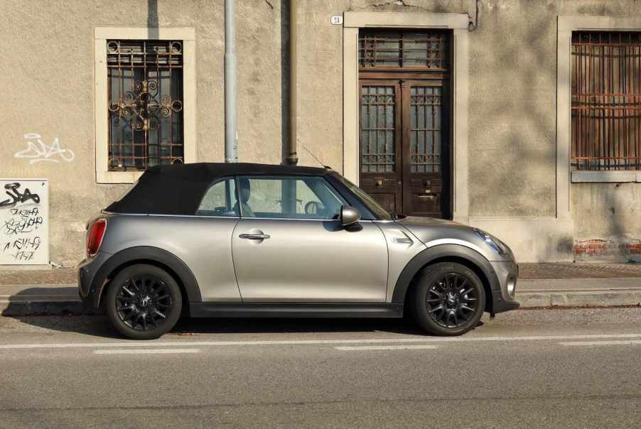 Gray mini cooper convertible with a black top parked on a city street.