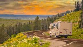 RV camper truck driving along a mountain road, the sun setting in the distance.