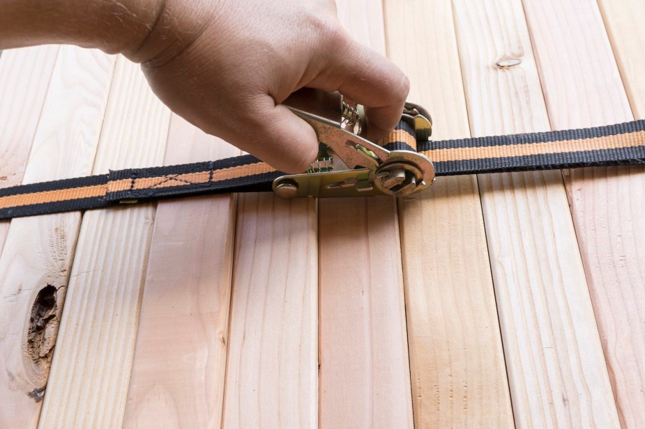 Closeup of a hand pulling the release trigger on a ratchet strap's mechanism.