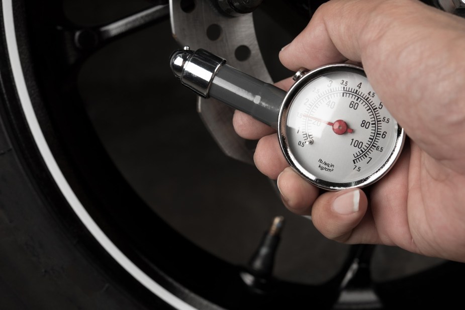 Man uses a tire pressure gauge to check his psi in hot summer weather.