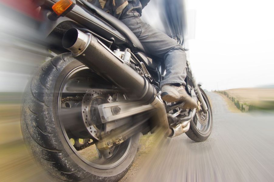 Closeup of a motorcycle riders foot and back tire, the background blurring by