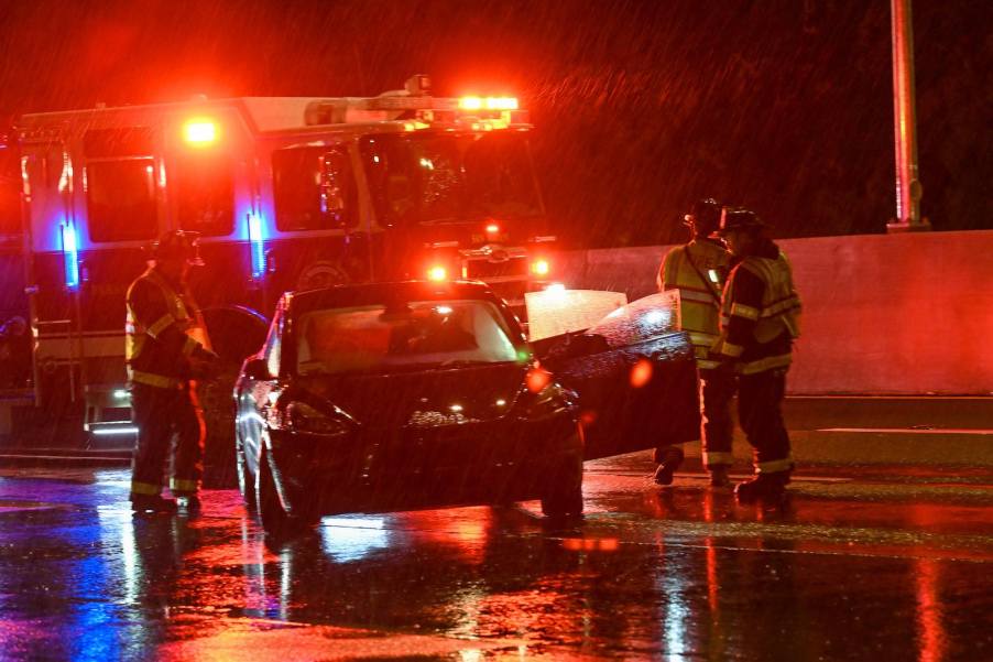 First responders gather around a crashed Tesla sedan parked on the interstate on a rainy night.