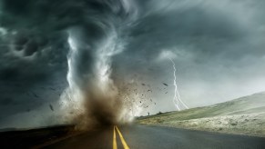 A tornado touches down on a rural road while lightning strikes in the distance