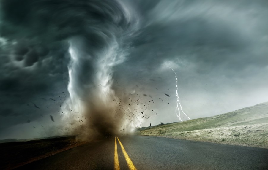 A tornado touches down on a rural road while lightning strikes in the distance