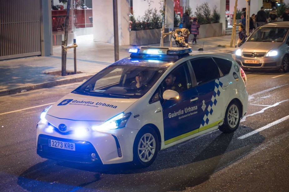 A yellow and blue Toyota Prius police cruiser driving in Barcelona.