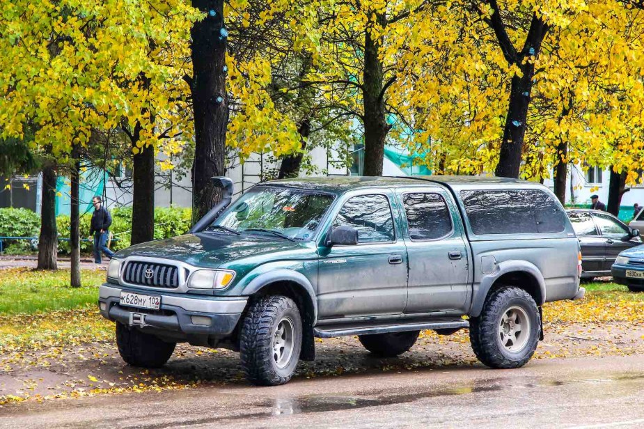 Dark green Toyota Tacoma parked in front of trees on a city street.