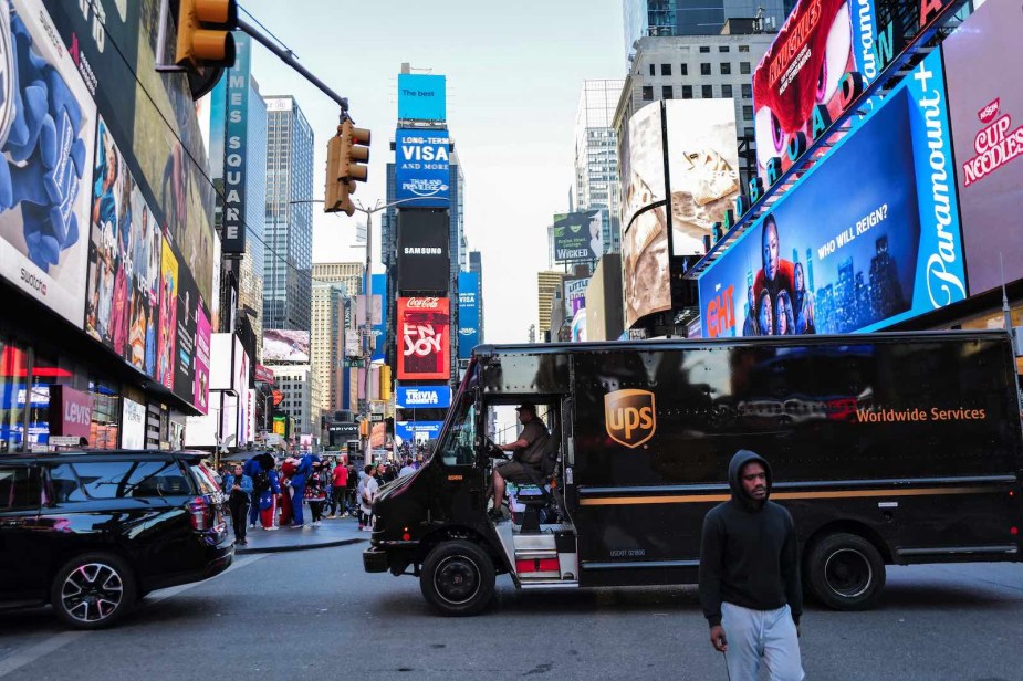 Brown UPS delivery truck navigating traffic in a crowded Tims Square in New York City