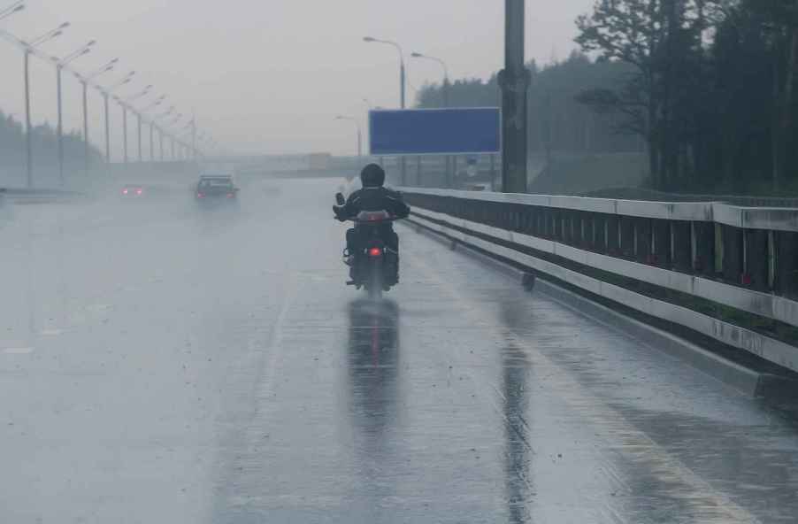 A biker riding a motorcycle away from camera on freeway in the rain