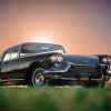 A black 1958 Cadillac Eldorado Brougham parked on grass in right front angle view with sun barely peeking over roofline